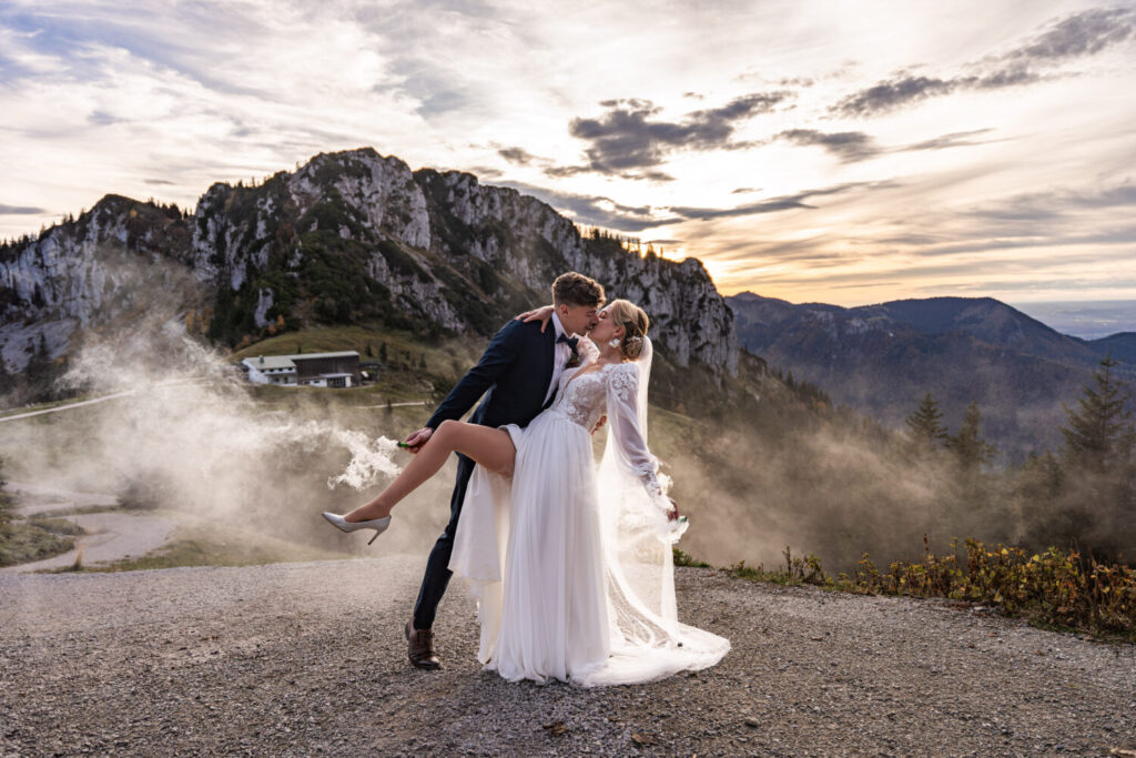 Brautpaar beim Hochzeitsshooting vor Bergpanorama auf Kampenwand in Bayern – natürliches Licht, moderne Reportage-Fotografie, Sonnenuntergang