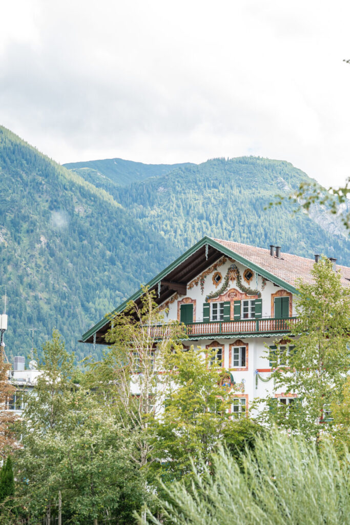 Traditionelles bayerisches Haus mit Lüftlmalerei und grünen Fensterläden vor grünem Bergpanorama
